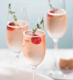 Coupe de bulles rosées garnie de framboises fraîches et d’une branche de thym.